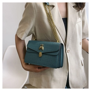 Gros plan sur le sac en relief crocodile sarcelle avec boucle abeille dorée et chaîne