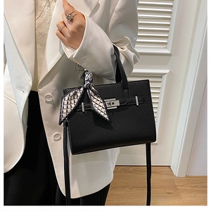 Détail du sac à main noir en cuir grainé avec fermoir rotatif en métal et foulard en soie