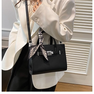 Détail du sac à main noir texture litchi avec fermoir rotatif argenté et foulard soyeux