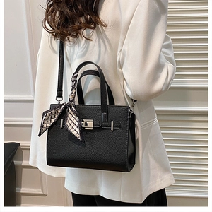 Sac à main noir avec motif litchi et foulard décoratif porté par un mannequin