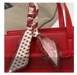 Détail de la poignée en cuir grainé rouge ornée d'un foulard twilly en soie à fleurs