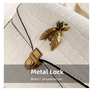 Gros plan sur le fermoir abeille dorée et la texture cuir crocodile du sac à main blanc