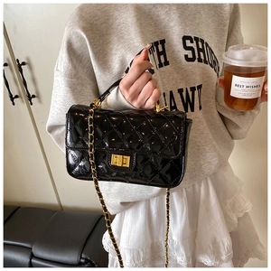 Detail of glossy black patent leather quilted handbag with gold chain strap and turn-lock