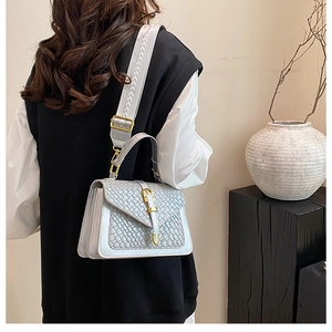 Detail of grey woven textured bag with gold clasp and embroidered shoulder strap
