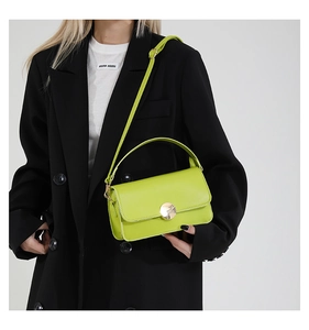 Détail du sac en cuir vert fluo avec boucle dorée sur un mannequin en blazer noir