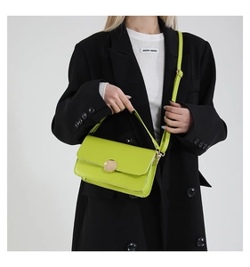 Détail du sac bandoulière vert fluo avec boucle dorée sur un blazer noir chic