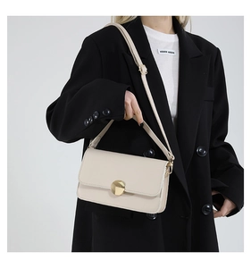 Close-up of minimalist cream leather crossbody bag with a large golden circular buckle