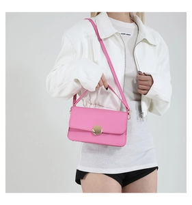 Gros plan du sac à main carré rose avec boucle dorée ronde sur une tenue blanche