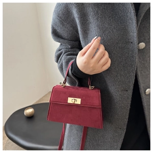 Détail du petit sac carré en daim bordeaux avec fermoir doré porté par le mannequin