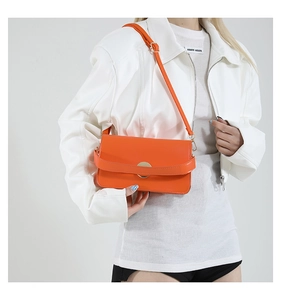 Close-up of bright orange crossbody bag with gold ring lock and sleek leather strap