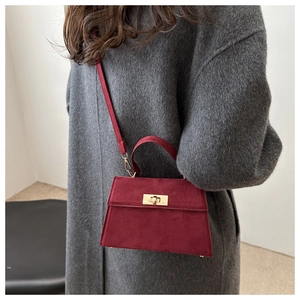Detail of burgundy suede crossbody bag with gold twist lock on grey wool coat