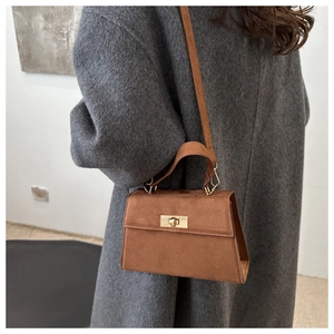 Détail du sac bandoulière en daim caramel avec fermoir rotatif doré sur manteau