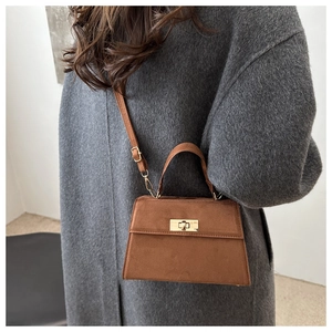 Detail of a brown matte crossbody bag with a gold twist lock on a wool coat