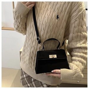Detail of black trapezoid crossbody bag with gold twist lock on knit sweater background