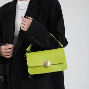 Sac à bandoulière vert fluo avec boucle dorée porté sur un blazer noir par un mannequin