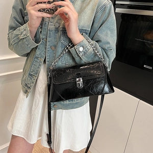 Sac bandoulière rétro en cuir verni noir avec chaîne argentée porté par un mannequin