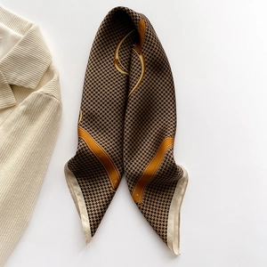 Detail of silk scarf showing deep brown houndstooth pattern and gold trim on white surface