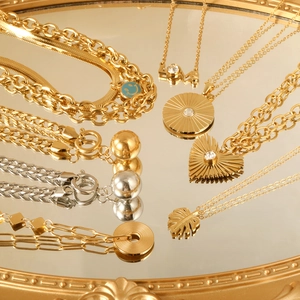 Golden heart and leaf pendant necklaces displayed on a mirror reflecting luxury style