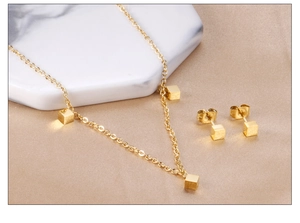 Détail d'un ensemble de bijoux dorés avec des pendentifs cubes mats sur marbre