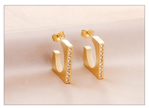 Detail of gold C-shaped earrings with micro-inlaid white zircons on satin background