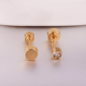 Detail of minimalist gold cylinder stud earrings with crystal inlay on a neutral surface