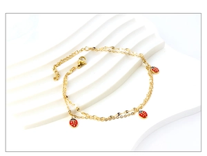 Detail of a gold-plated anklet featuring red enamel ladybug charms on a double-layer chain