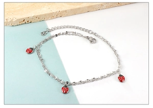 Detail of stainless steel anklet featuring three colorful red enamel ladybug charms