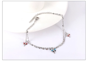 Detail of silver layered anklet featuring colorful dragonfly pendants and lobster clasp