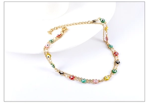 Macro detail of gold anklet with multi-colored enamel evil eye beads on white display
