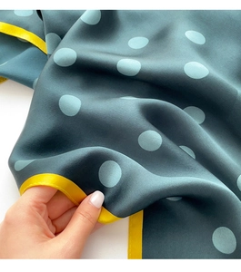 Detail of silk scarf showing dark green fabric with blue polka dots and yellow edges
