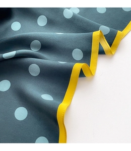 Close-up of silk scarf with light blue dots on dark teal fabric and yellow edges