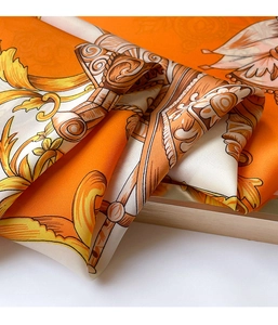 Detailed close-up of orange silk scarf with gold baroque patterns and luxury texture