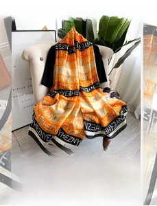 Détail d'un élégant foulard en soie orange avec imprimé lettres posé sur une chaise