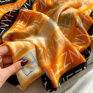 Détail d'un foulard en soie avec imprimé lettres orange et noir et texture brillante