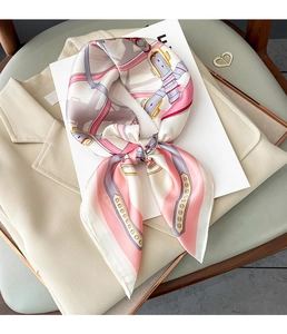 Détail du foulard en soie à motifs rose et argent sur un blazer beige avec broche dorée