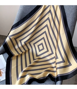Close-up of yellow silk scarf with geometric black and white square pattern on grey fabric