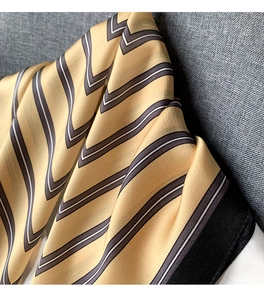 Close-up of silk scarf showing yellow and black geometric chevron stripes and soft satin sheen