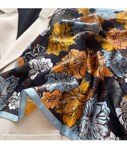 Detailansicht eines eleganten Seidenschals mit Blumenmuster auf einem beigen Blazer