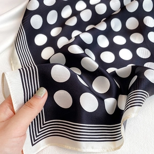 Detail shot of black and white polka dot silk scarf showing soft satin texture and drape