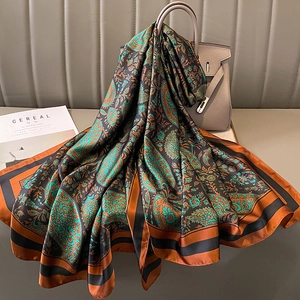 Detail of paisley silk scarf in teal and orange draped over a luxury leather handbag
