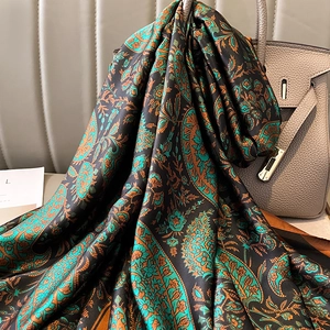 Detail of teal paisley pattern silk scarf draped over a luxury leather handbag