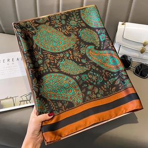 Elegant paisley satin scarf with blue and orange tones draped over a grey leather surface