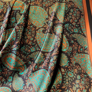Detailed view of luxurious paisley pattern scarf with silky peacock green and orange tones