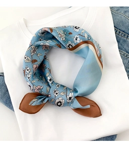 Détail d'un foulard en soie floral bleu clair noué sur un t-shirt blanc épuré