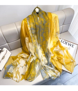 Detail of elegant yellow and gray floral silk scarf draped on a soft gray sofa