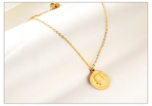 Gros plan d'un collier pendentif pièce dorée avec fermoir mousqueton sur satin blanc