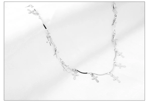 Détail de breloques en forme de croix argentées sur une chaîne de collier minimaliste