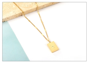 Close-up of gold rectangular sun pendant with zircon on a textured stone surface