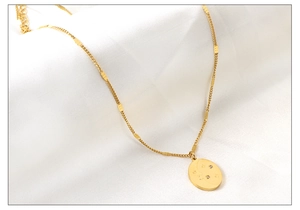 Detail of gold oval pendant with celestial star moon motifs on a white fabric background