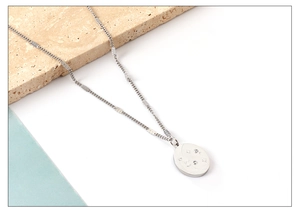 Macro detail of oval stainless steel pendant with star engraving and small crystals